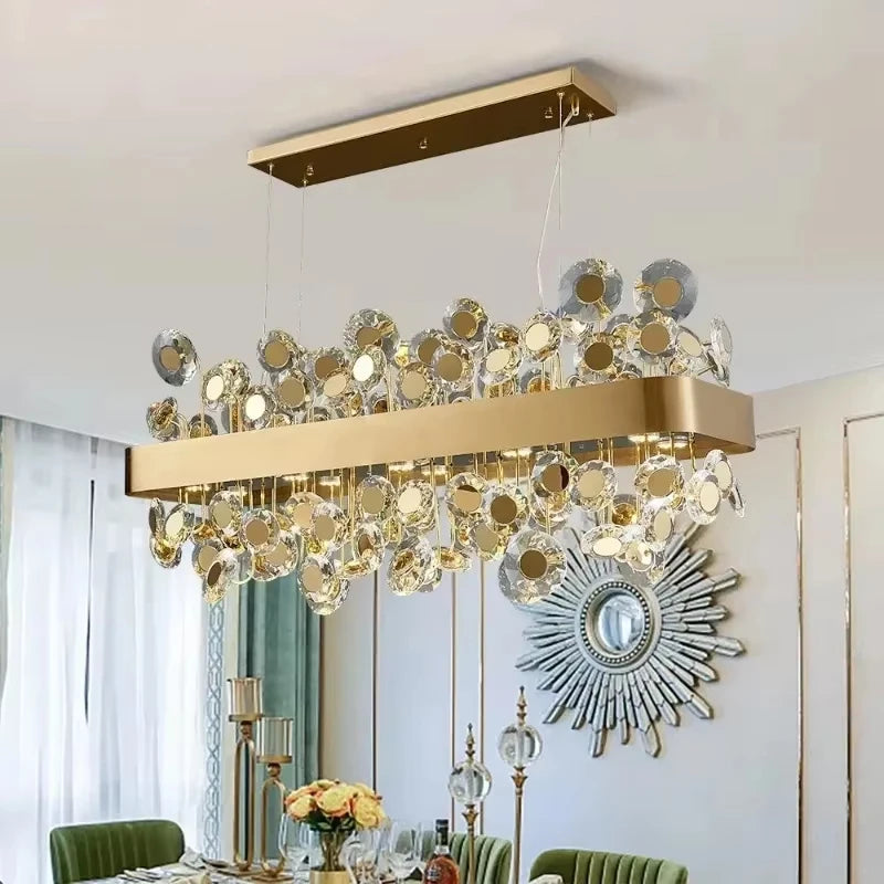 Rectangular gold chandelier with clear and gold-toned crystals, installed in a dining room with a sunburst mirror on the wall.