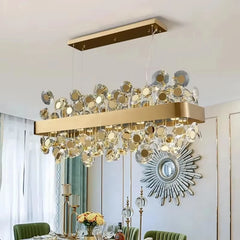 Rectangular gold chandelier with clear and gold-toned crystals, installed in a dining room with a sunburst mirror on the wall.