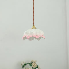 A side view of a pink and white ceramic petal pendant light with pearl accents, hanging against a white wall.