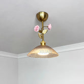 A gold pendant light with a textured amber glass shade and a decorative stem featuring two pink ceramic roses and gold leaves, mounted on a white ceiling.