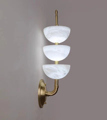 Wall-mounted light fixture with three white glass shades and gold metal arm on a gray background