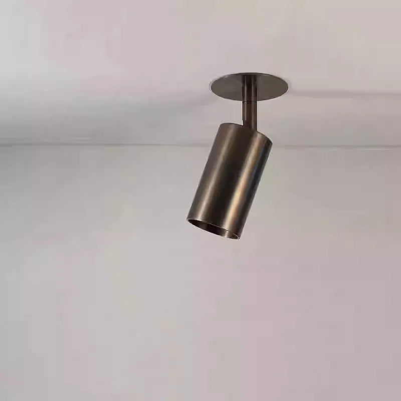 A close-up of a dark brushed metal cylinder spotlight mounted on a white ceiling, showing its angled position.