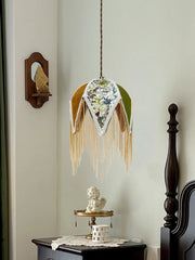 Decorative wall hanging with fringes and a small statue on a shelf against a light green wall.