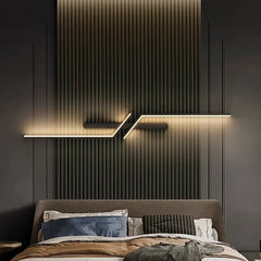 A contemporary bedroom setting with two gold geometric wall sconces mounted on a textured dark wall above nightstands.