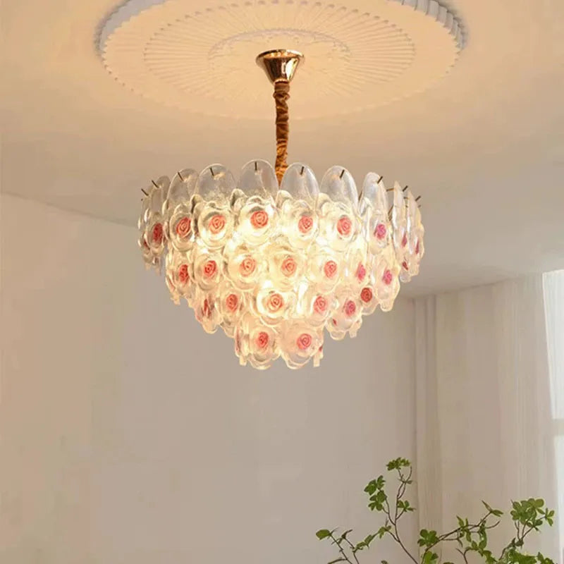 Brushed gold chandelier with clear glass and pink rose accents, in a close-up view.