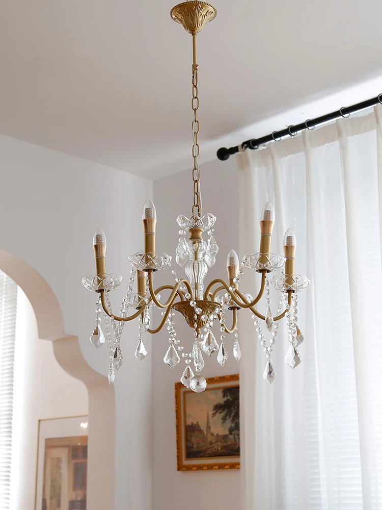 Gold chandelier hanging in a room with white curtains and wall art.