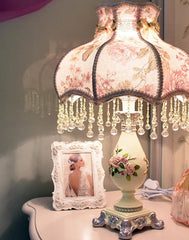 Decorative table lamp with pink floral shade on a table.