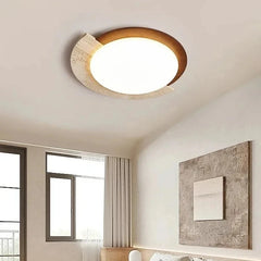 An oval flush mount ceiling light with natural stone and wood accents installed in a bedroom setting above a bed.