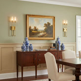 A contemporary gold metal wall sconce with a curved arm and a frosted acrylic cylinder shade, mounted on a pale green wall.
