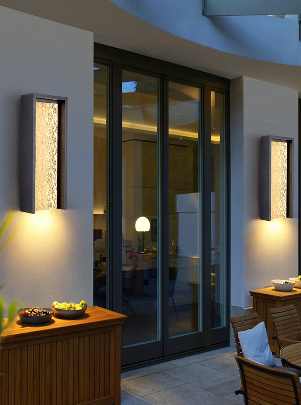 Modern outdoor setting with wall lights, glass doors, and wooden furniture.