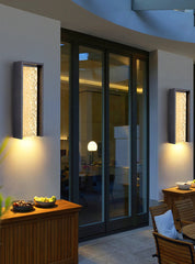 Modern outdoor setting with wall lights, glass doors, and wooden furniture.