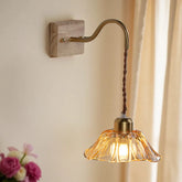Wall-mounted lamp with glass shade and wooden base on a neutral wall.