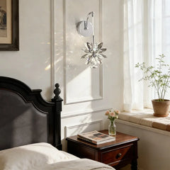 A bedroom scene with a dark wood bed and nightstand, a window with sheer curtains, and a wall sconce with a crystal flower design casting light.