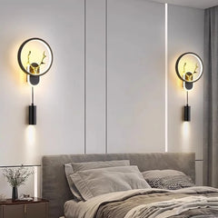 Two black wall sconces with circular LED halos and integrated antler designs, mounted on a bedroom wall above a bed.