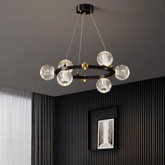 Modern chandelier with crystal balls hanging from a ceiling in a room with dark walls and a window.