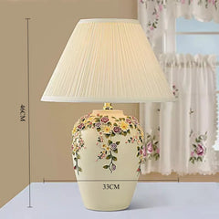 Decorative table lamp with floral design and pleated shade on a neutral background