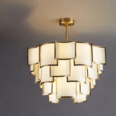 A multi-tiered pendant light with square frosted glass shades and a gold frame, illuminated against a gray ceiling.