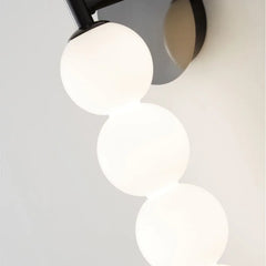Close-up of a modern ceiling light fixture with three spherical white lights on a neutral background.