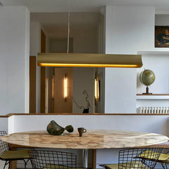 Modern kitchen with a long gold pendant light above a marble table.