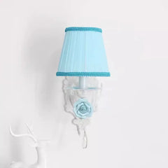 Close-up of a single white wall sconce with a blue pleated fabric shade, blue rose accent, and crystal droplet.