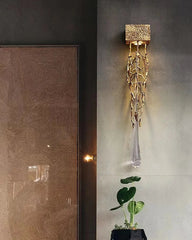 Decorative wall light fixture on a gray wall with a plant in the foreground.