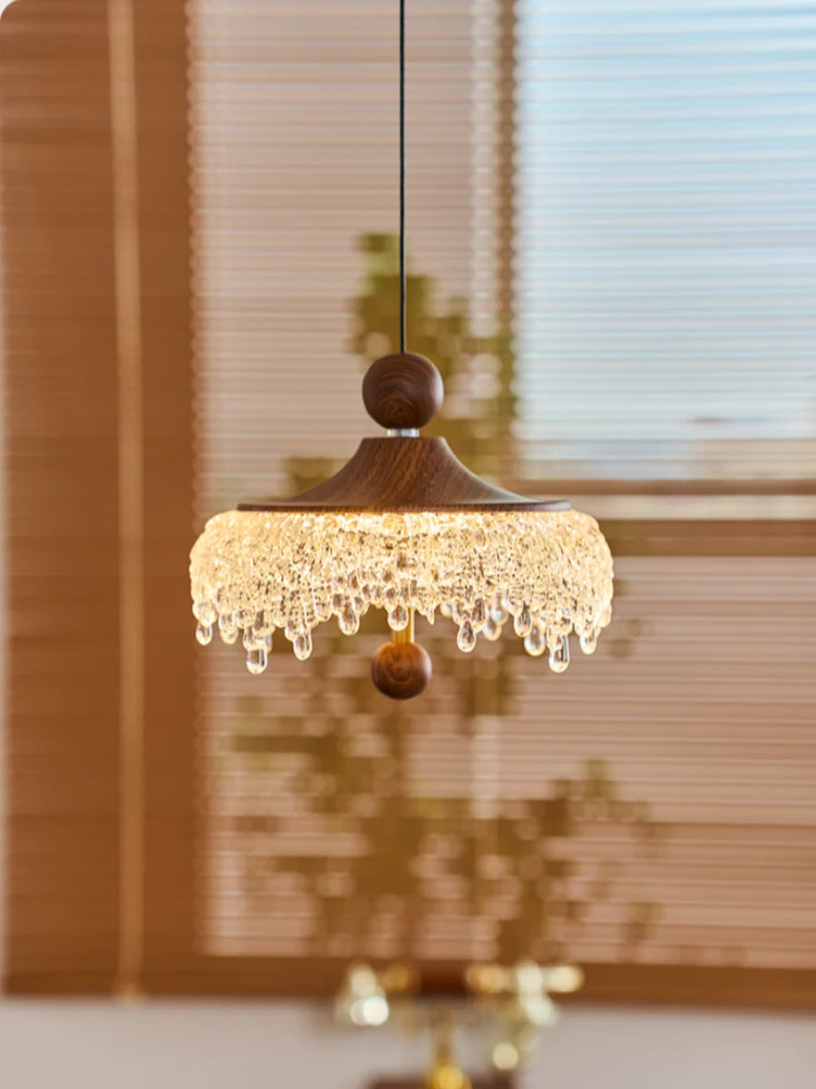 Decorative pendant light with wooden shade and crystal details in a room setting.