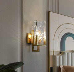 Decorative wall sconce with glass shade on a wall next to a mirror.