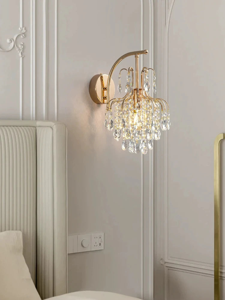 Gold crystal wall sconce mounted above a tufted headboard in a bedroom setting.