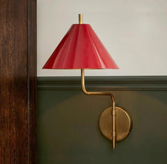 Wall-mounted lamp with red shade and gold arm on a green wall.