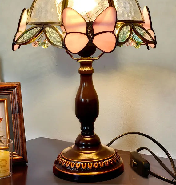 Decorative table lamp with butterfly design on a surface next to a framed picture and candle.