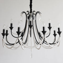 A black, multi-arm chandelier adorned with strings of white pearl-like beads and clear crystal teardrops, featuring candelabra-style light sockets against a plain white background.