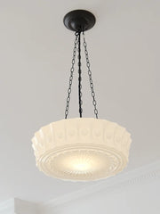 Close-up view of a cream decorative glass pendant light with a black chain against a white ceiling.