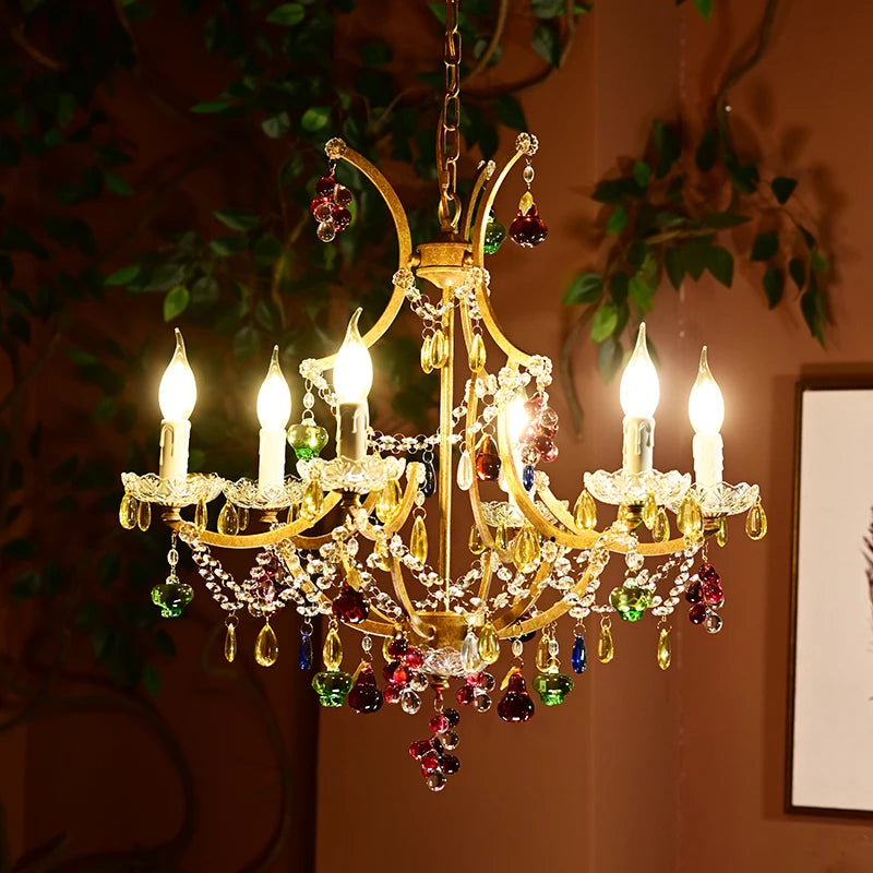 A gold chandelier with crystal embellishments is displayed in a room with dark walls and greenery.