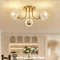 A polished gold semi-flush ceiling light with two ripple glass globes and a central crystal accent, illuminating a dining area with a table and chairs.
