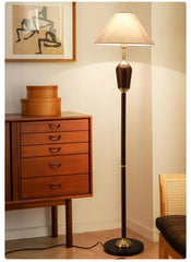Floor lamp next to a wooden dresser with a painting on the wall.