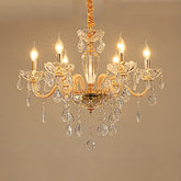 Close-up of a gold crystal chandelier with multiple arms and dangling crystals, illuminated against a plain background.