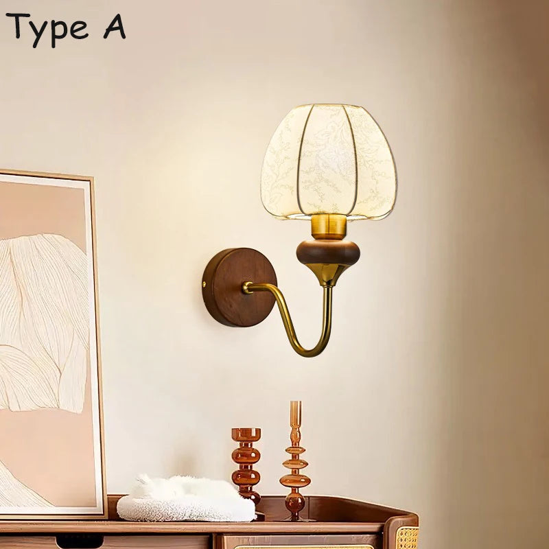 Wall sconce with a round wooden base, a curved brass arm, and a bell-shaped glass shade in a room setting.