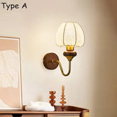 Wall sconce with a round wooden base, a curved brass arm, and a bell-shaped glass shade in a room setting.