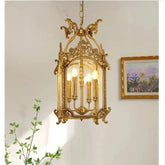 A gold candelabra-style pendant light with a decorative cage frame, hanging in a well-lit room with a painting on the wall.