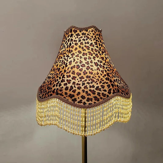 Close-up of a leopard print fabric bell lampshade with gold and cream beaded fringe hanging down.