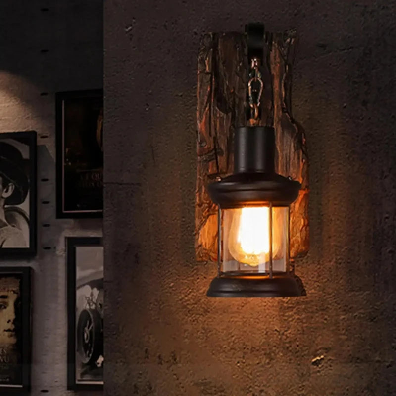 Close-up of a black iron lantern wall sconce with a distressed wood backplate mounted on a textured gray wall, with framed art on the left.