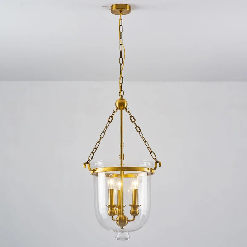 Polished copper and clear glass drum pendant light hanging from a chain against a white ceiling