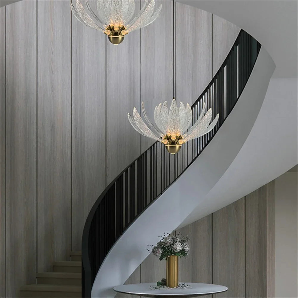 Two clear acrylic lotus flower pendant lights hanging near a curved staircase with wooden walls and a black railing.