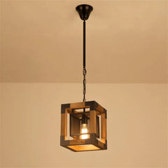 Square industrial pendant light with wood frame and dark metal cage, featuring one exposed bulb suspended by a chain from a ceiling canopy.