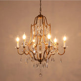 A close-up of a gold crystal candelabra chandelier with six illuminated bulbs against a light brown background.