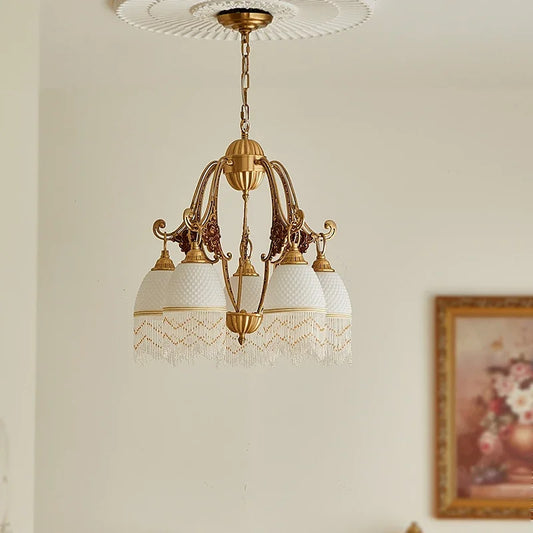 Close-up of a polished brass chandelier with white glass shades and decorative bead fringe, featuring ornate floral ceramic accents on the arms, mounted on a white ceiling medallion.