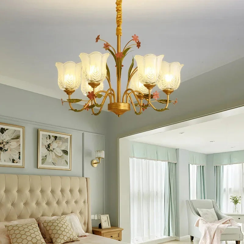 A gold floral ceramic chandelier with glass shades positioned above a bed in a bedroom.