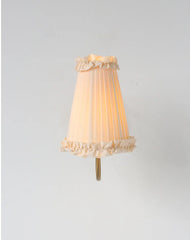 French retro wall lamp with pleated fabric shade and brass arm mounted on white wall