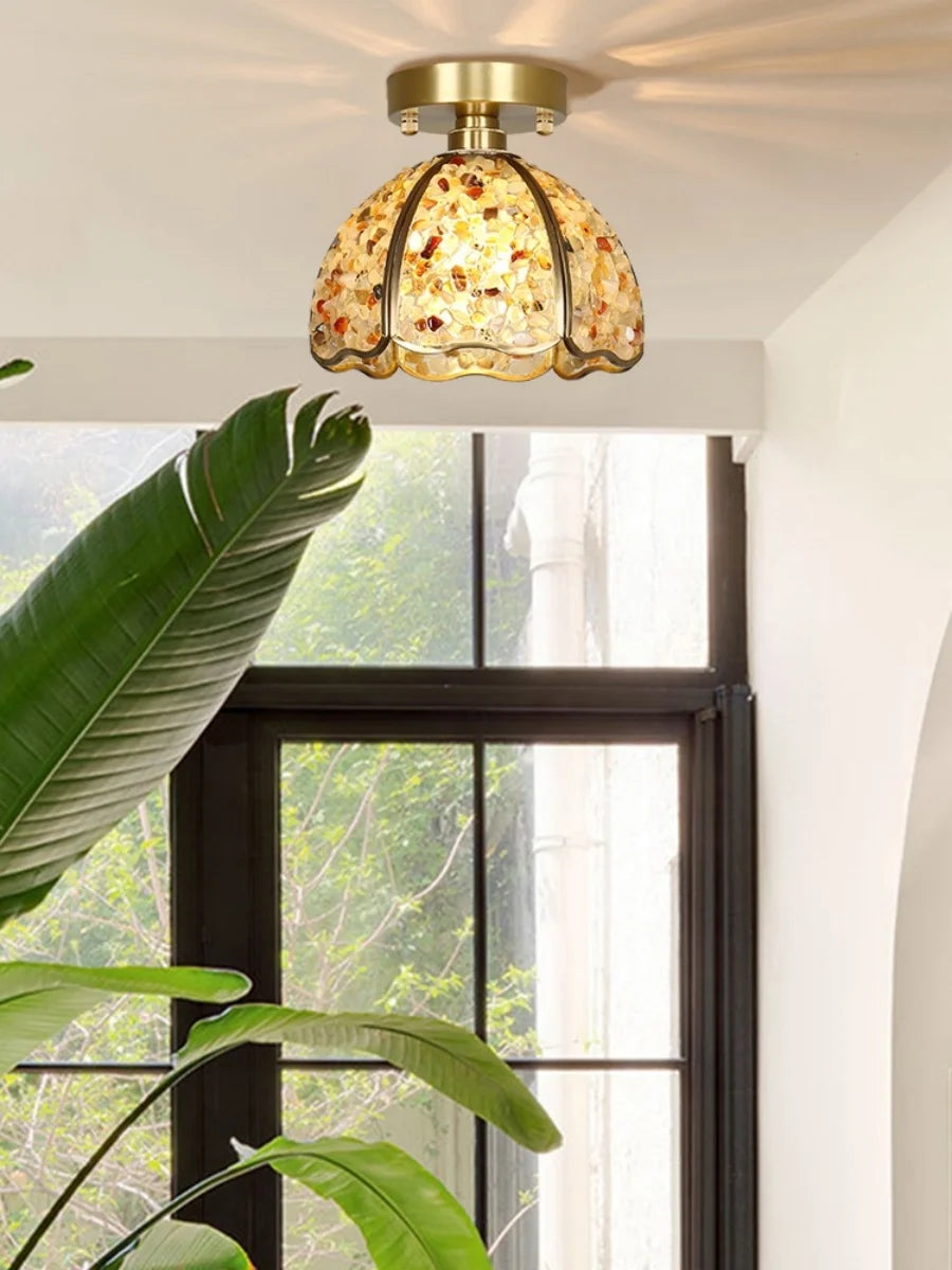 Decorative ceiling light fixture with mottled glass shade in a room with a window and plants.