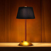 Table lamp with black shade and gold base on a wooden surface.